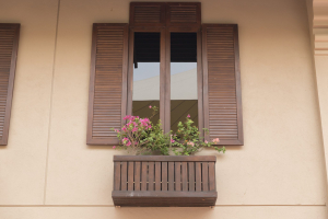 A shuttered tinted window on a brown building with a flower ledge