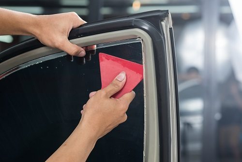 Skilled worker applying window tints on car door.